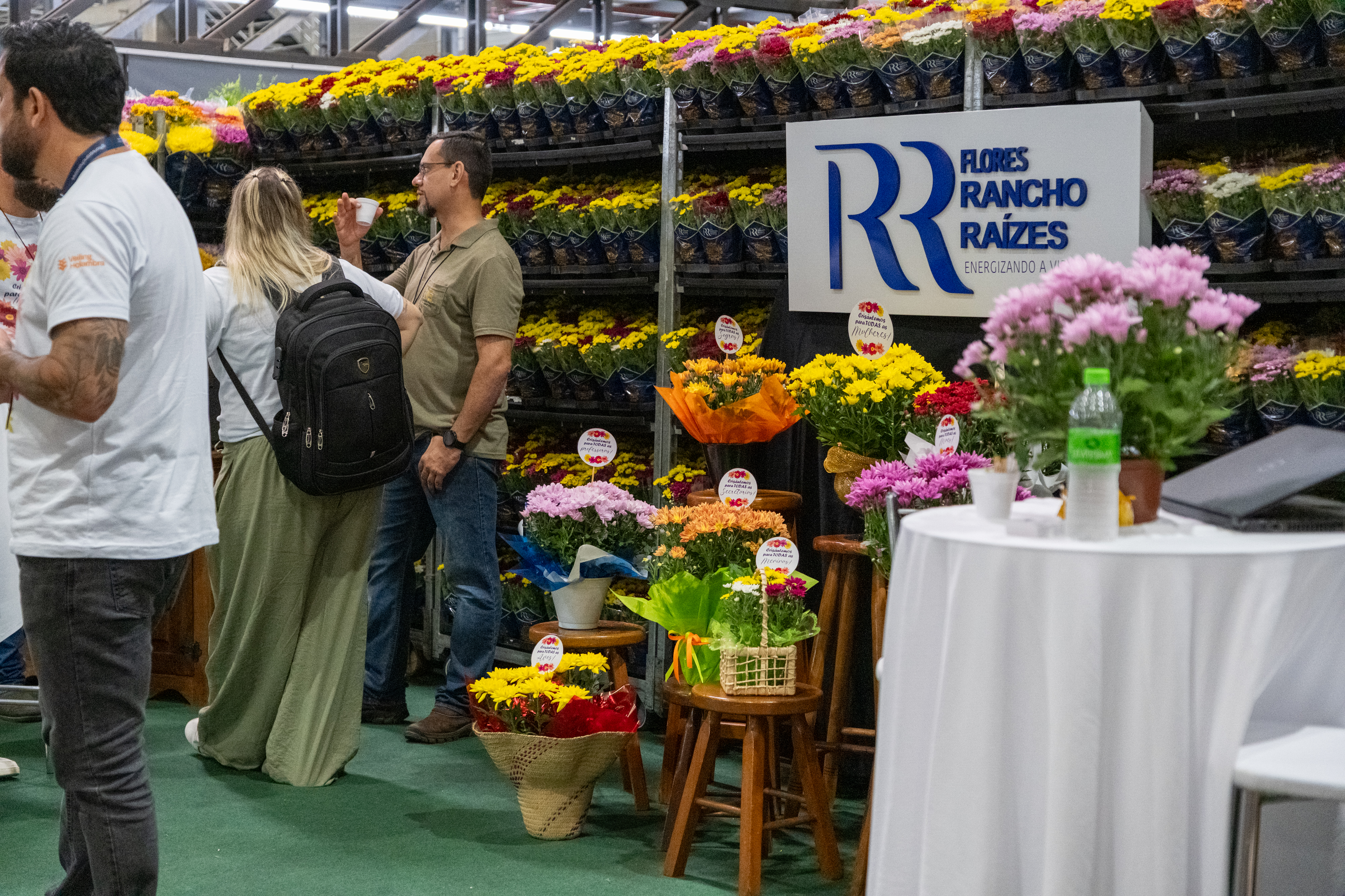 Compradores e lojistas em negociação em estande repleto de vasos de flores no Veiling Market
